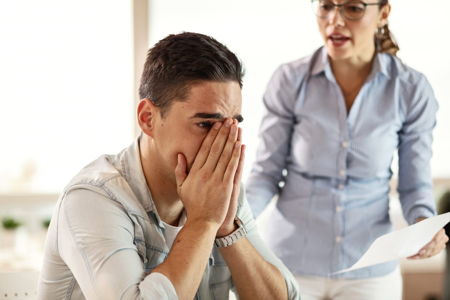 Young businessman feeling depressed while being criticized by bossy businesswoman. Stressed businessman feeling sad while his female boss is scolding him at work.